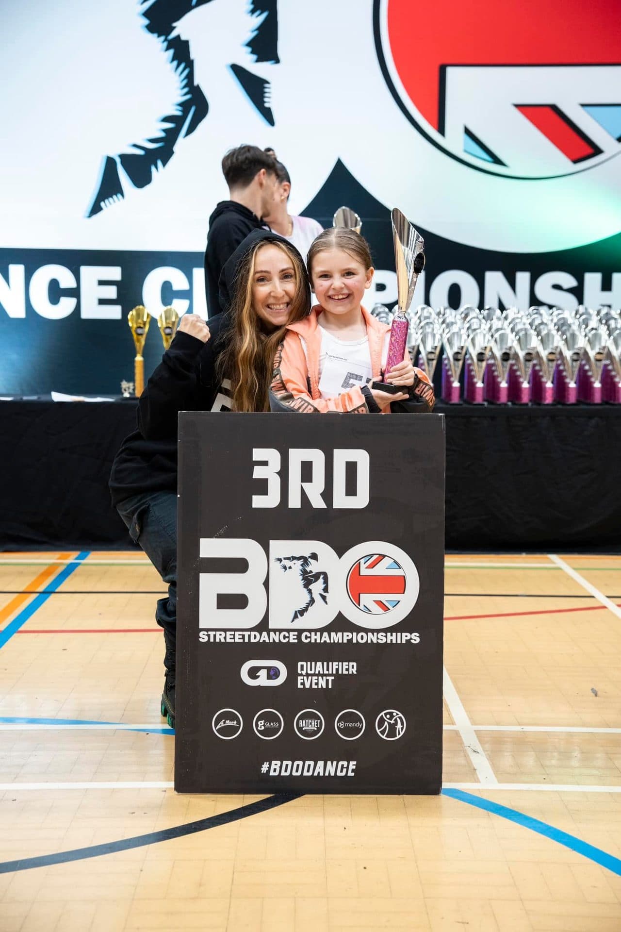 Young D2E dancer holding a 3rd place trophy alongside her teacher at the BDO Championships